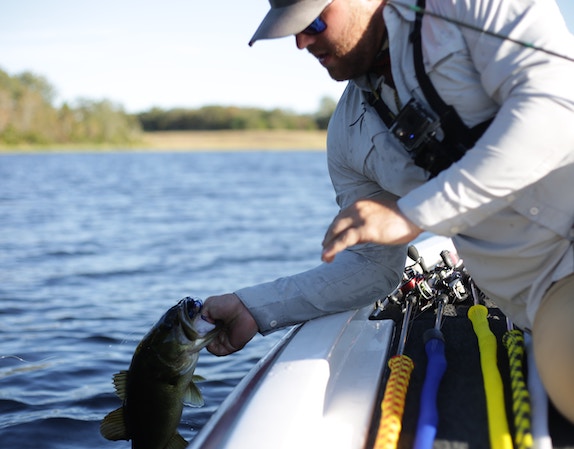 a fisherman on a boat releasing a fish into the lake